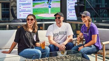 Kolme ihmistä istuu sohvalla, ja heidän takanaan televisiossa näkyy baseball-ottelu.