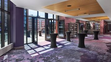 A modern lobby with large glass doors, a patterned carpet, and a ceiling with wooden panels.