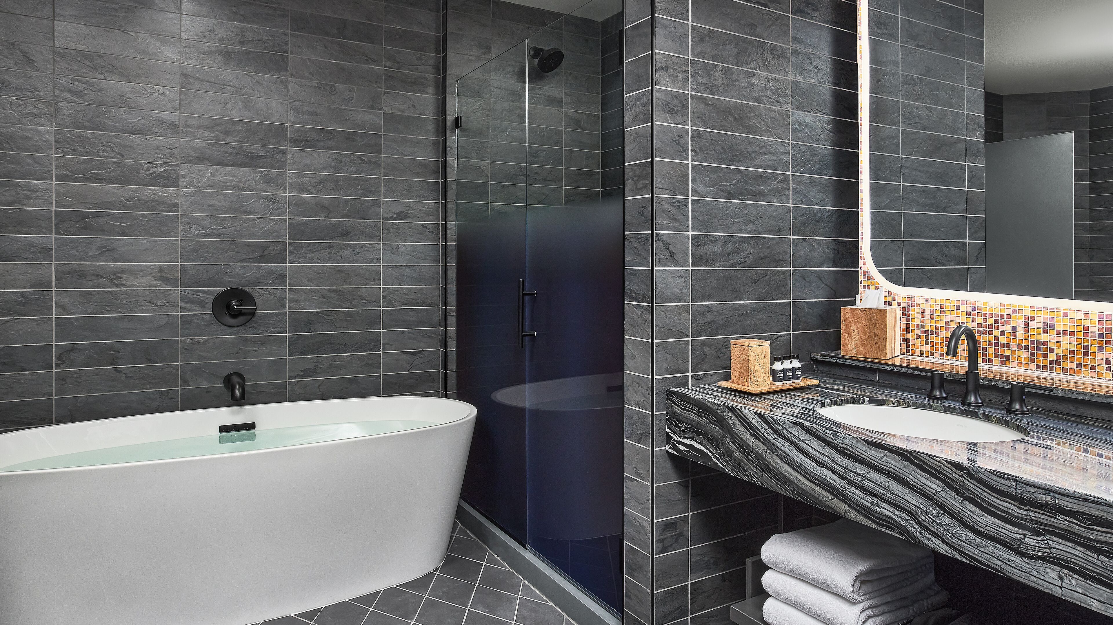 Een moderne badkamer met een vrijstaand bad, een douche met glazen wanden en een wastafel met een backsplash van mozaïektegels.