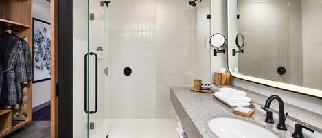 A modern bathroom with a glass-enclosed shower, a large mirror, and a granite countertop with a sink and towel rack.