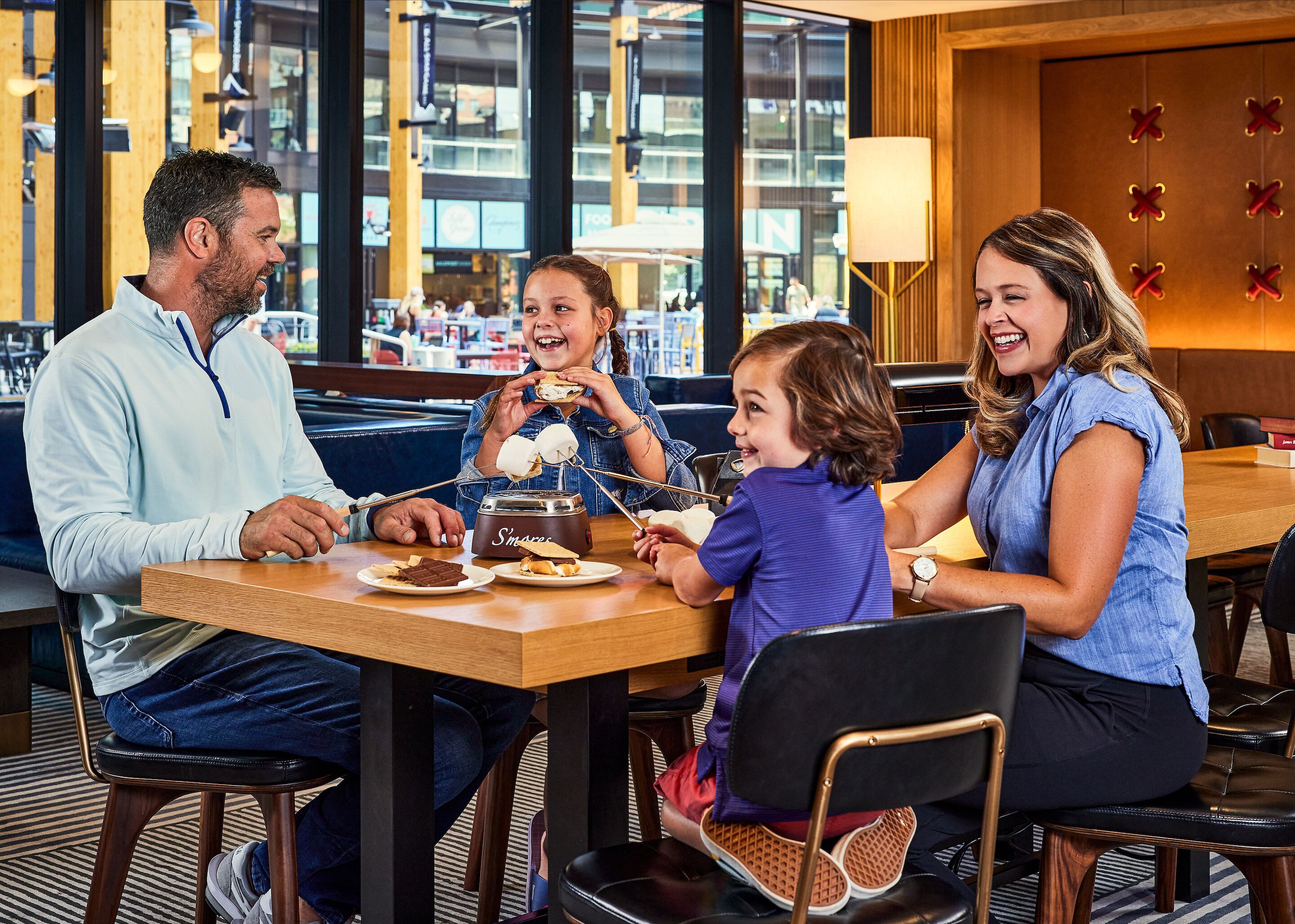 Une famille est assise à une table dans un restaurant, et de grandes fenêtres offrent une vue sur la ville.