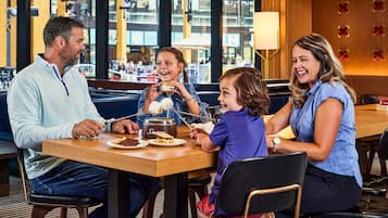 Une famille est assise à une table dans un restaurant, et de grandes fenêtres offrent une vue sur la ville.