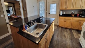 Una cocina con armarios de madera, encimera negra, pileta de acero inoxidable y ventilador de techo.