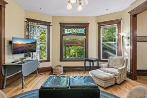 Una habitación con televisión, escritorio, silla y ventana con vistas a zonas verdes.