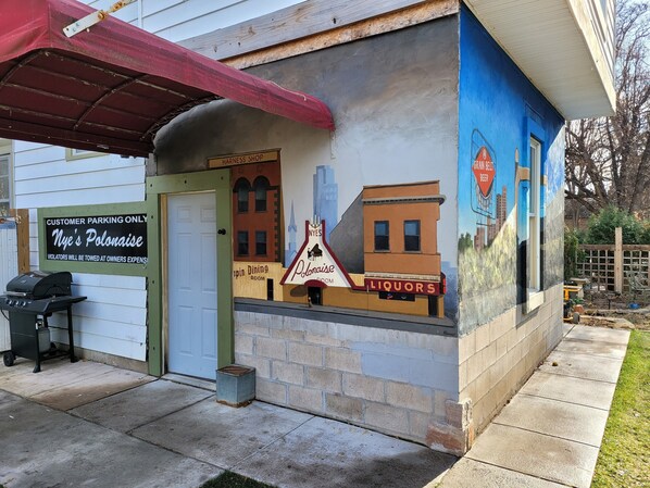 Un edificio con un mural de un paisaje urbano, un letrero de 'Harness Shop' y un letrero que dice 'Solo Estacionamiento para Clientes'.
