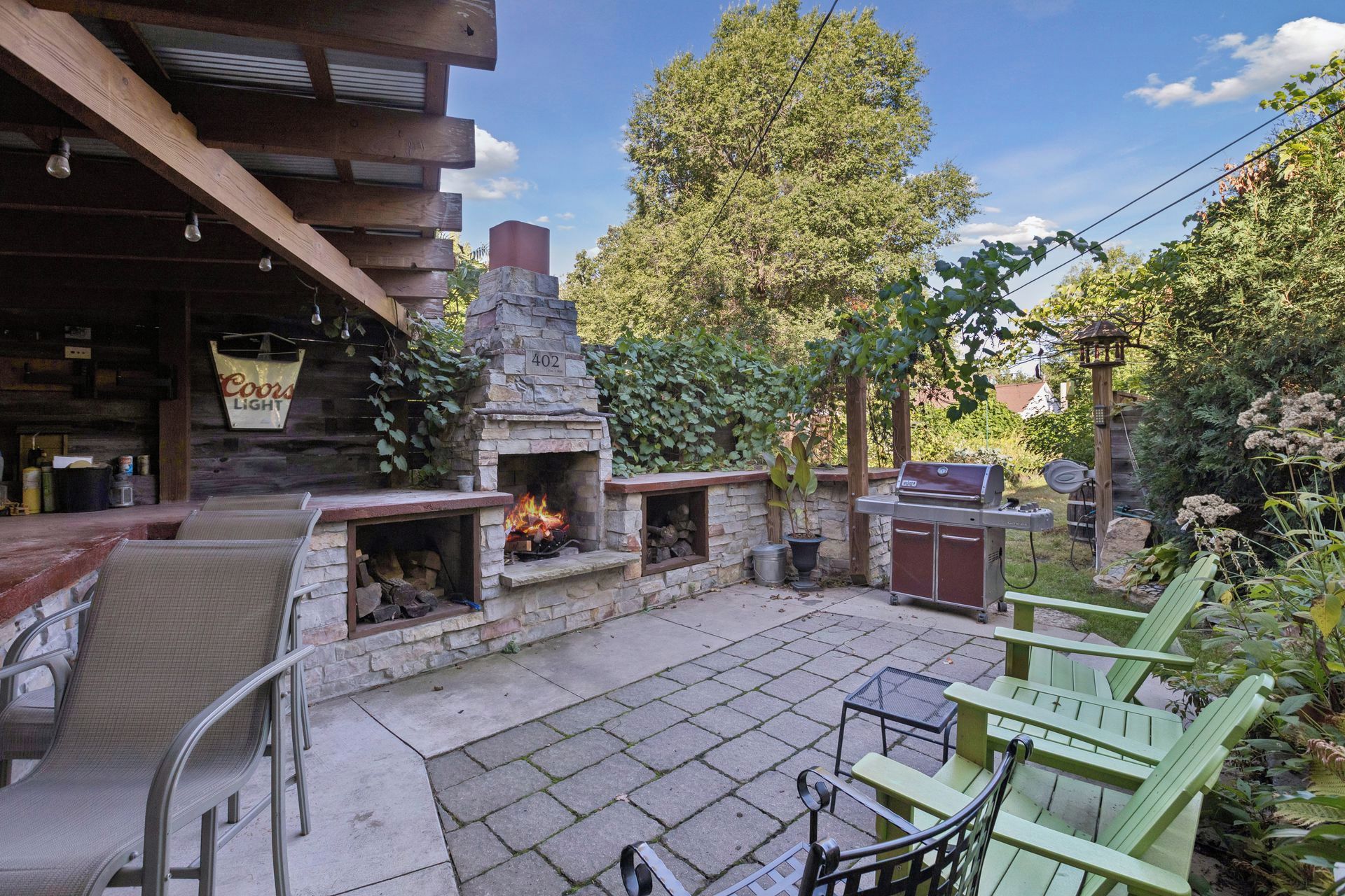 Un patio exterior con chimenea de piedra, sillas verdes y un letrero de Coors Light.