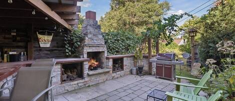 Un patio exterior con chimenea de piedra, sillas verdes y un letrero de Coors Light.