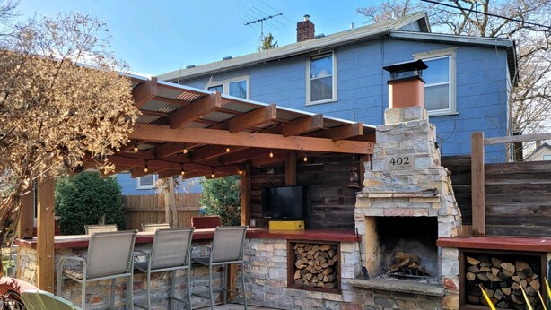 Un patio con mobiliario exterior, una chimenea de piedra y un televisor montado en la pared.