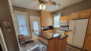 Una cocina con armarios de madera, lavavajillas de acero inoxidable, refrigerador blanco y ventilador de techo.