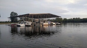 Un edificio grande con estructura metálica, rodeado de agua tranquila y barcos.