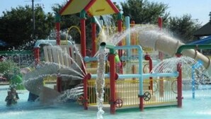 Un espace de jeux aquatiques doté de plusieurs jets d’eau et de toboggans, le tout étant entouré d’une clôture.
