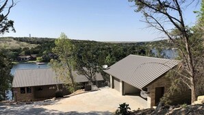A residential property with a paved driveway, a brick house with a sloped roof, and a view of a lake and hills in the background. - Welcome to Gemstone at Possum Kingdom Lake (Graford)