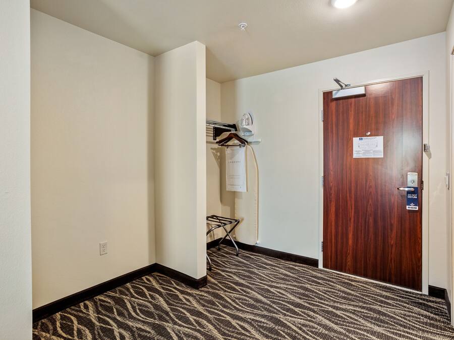 A hallway with a patterned carpet, a wooden door with a sign, and a wall-mounted drying rack.