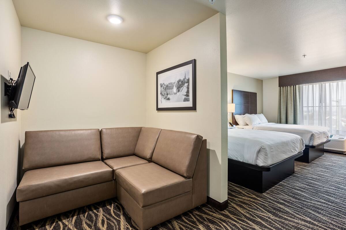 Habitación de hotel con sofá, dos camas, un cuadro enmarcado en la pared y una ventana con cortinas.