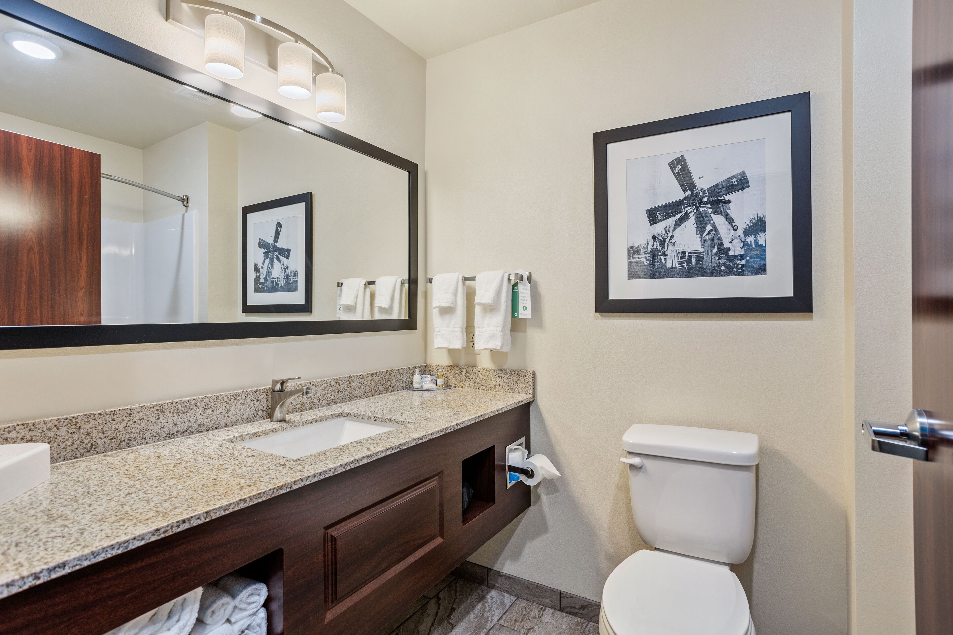 Une salle de bain avec deux lavabos, des toilettes, un grand miroir et des tableaux encadrés au mur.