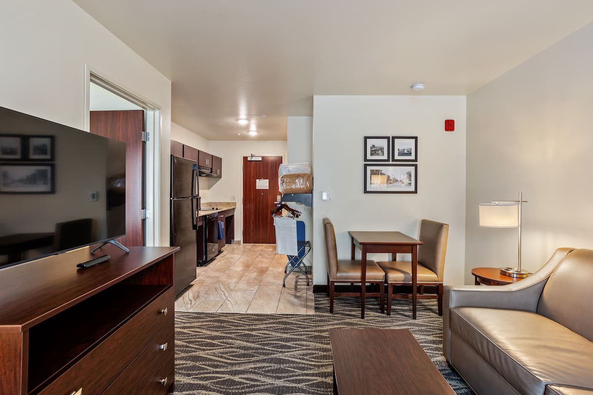 Una habitación de hotel moderna con televisión, sofá, mesa de comedor y zona de cocina.