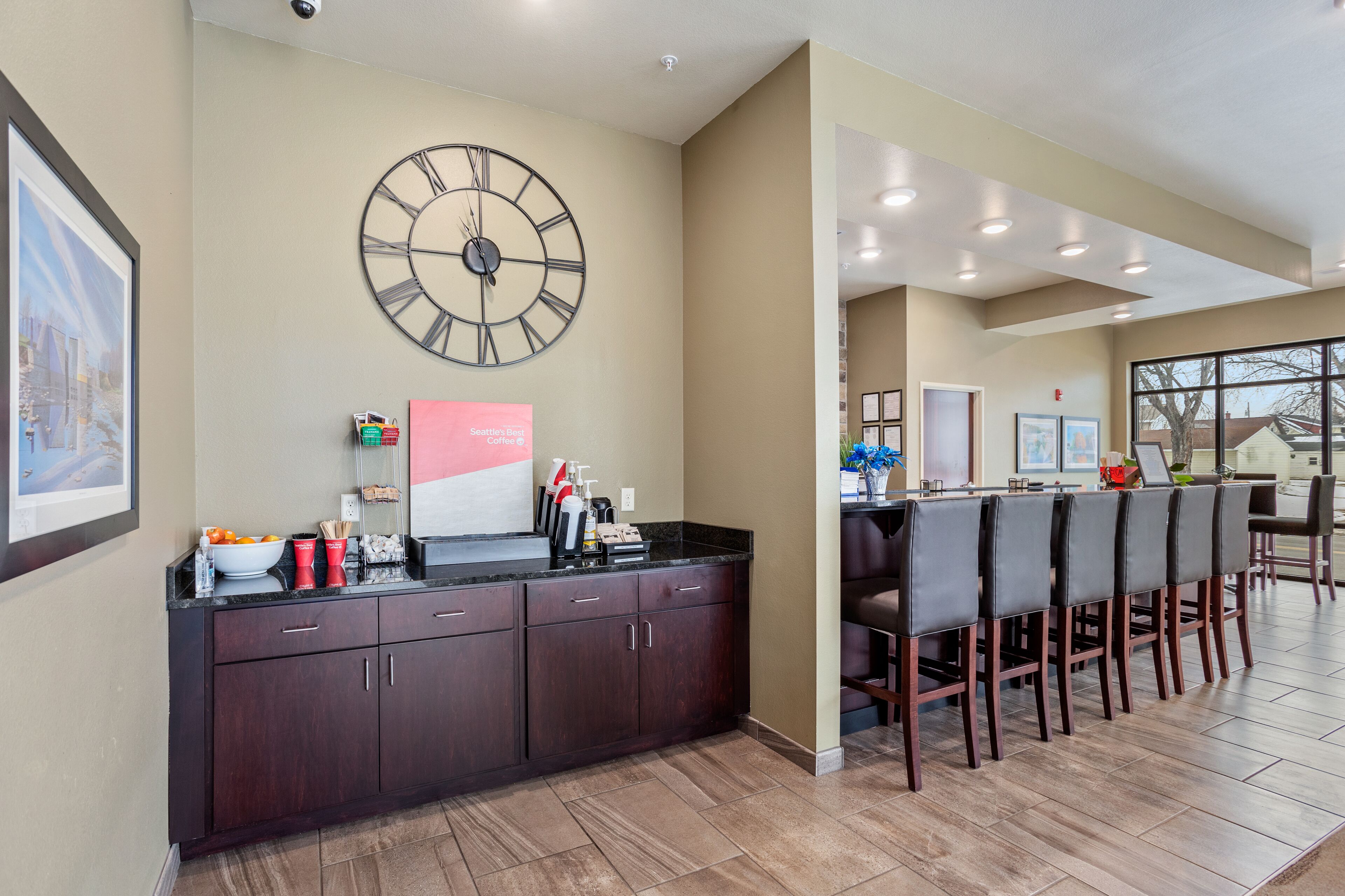 A modern kitchen with dark wooden cabinets, a large wall clock, and a bar area with bar stools.