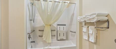 A bathroom with a shower, a bathtub, a towel rack, and a towel dispenser.