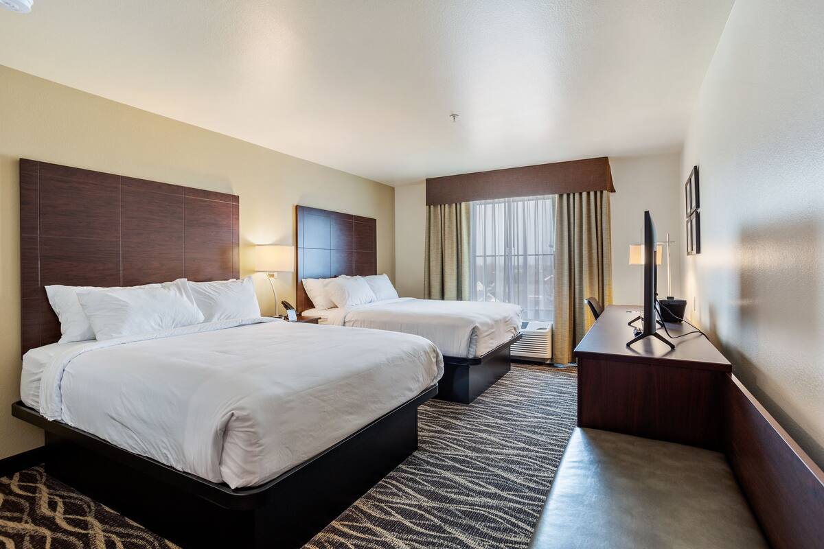Habitación de hotel con dos camas, un escritorio, una silla, una lámpara y una ventana con cortinas.
