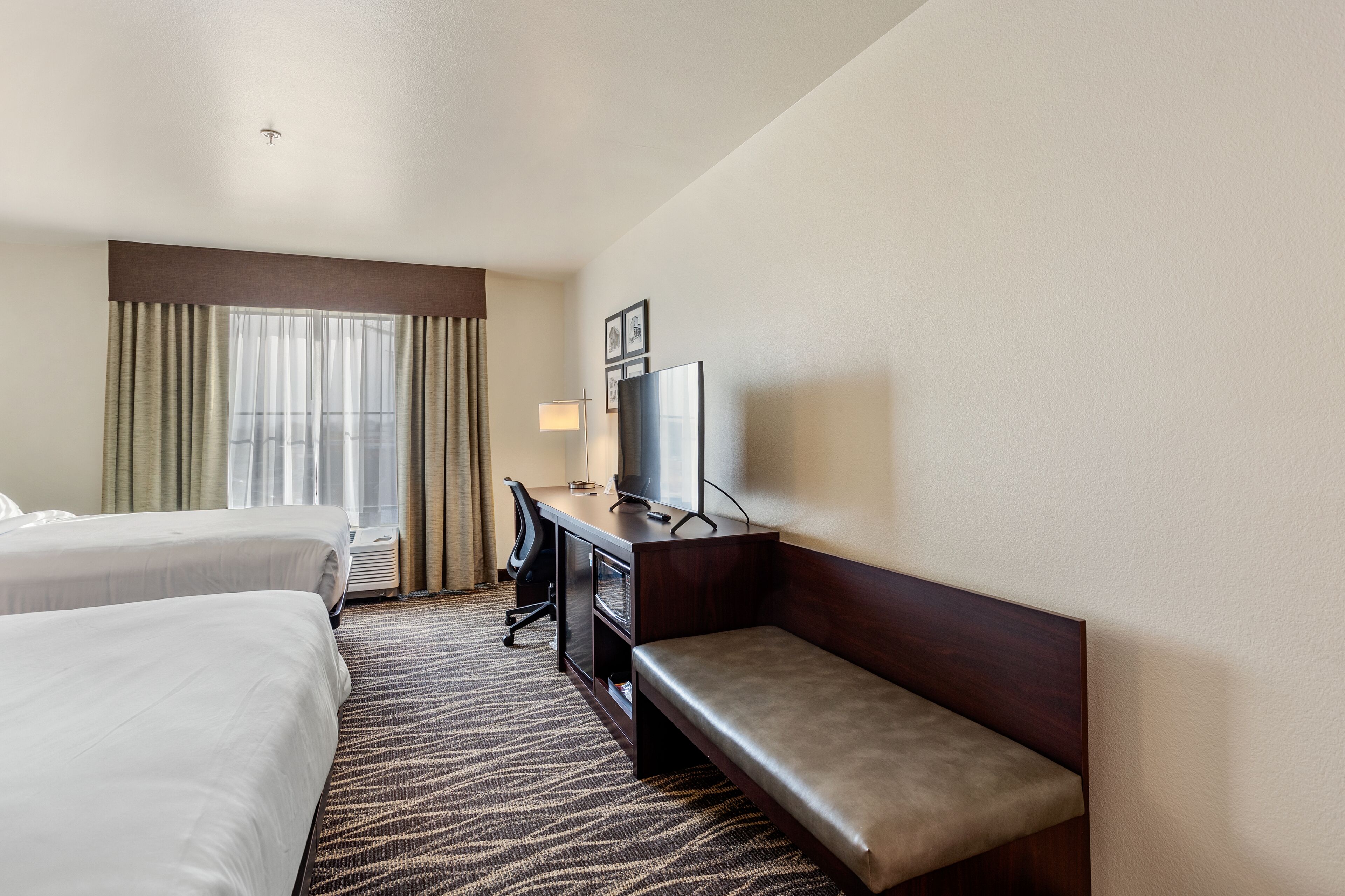 Habitación de hotel con dos camas, un escritorio con silla, televisión y ventana con cortinas.