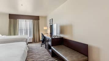 Habitación de hotel con dos camas, un escritorio con silla, televisión y ventana con cortinas.