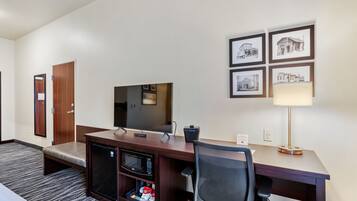 A hotel room with a desk, a television, a microwave, a mini-fridge, a chair, and a bed.
