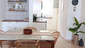 A modern kitchen with white cabinets, a dining area with a glass table and wicker chairs, and a potted plant. - Cozy 2 Bdrms Condo Apt Few Steps from the Beach (Río Grande)