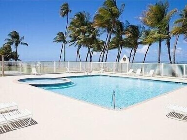 A rectangular swimming pool with a white deck, surrounded by white lounge chairs and a white fence.