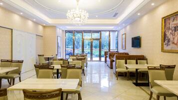 A spacious dining area with tables and chairs, a chandelier, and large windows offering a view of the outdoors.