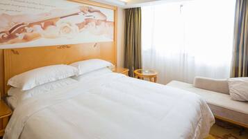 A hotel room with a large bed, a sofa, a small round table, and a large window with curtains.
