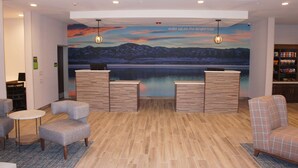 A reception area with a wooden reception desk, two armchairs, a small round table, and a mural of a lake with mountains.
