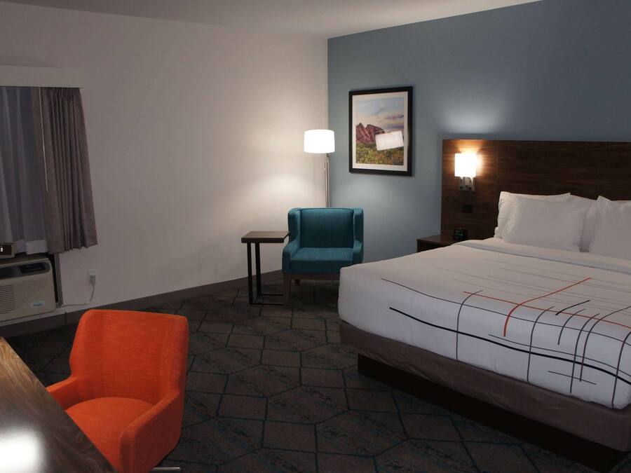 A hotel room with a bed, a desk, a chair, a lamp, and a painting on the wall.