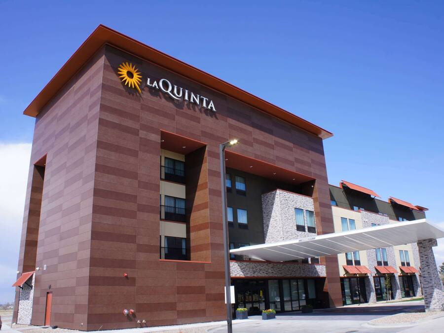 A La Quinta hotel with a modern design, featuring a prominent sun logo, a covered entrance, and a multi-story structure with visible windows and balconies.