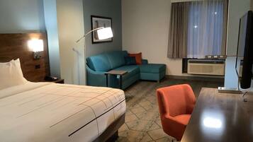 A hotel room with a bed, a desk, a chair, a sofa, a lamp, a picture on the wall, and a window with curtains.