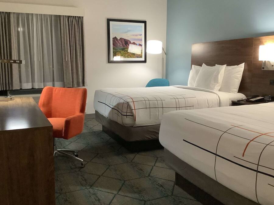 A hotel room with two beds, a desk, a chair, a lamp, and a painting on the wall.