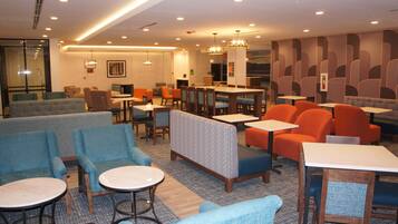 A modern hotel lobby with seating areas, tables, and a bar.