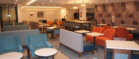 A modern hotel lobby with seating areas, tables, and a bar.