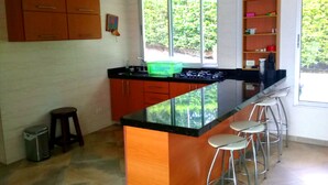 A kitchen with wooden cabinets, a black countertop, a green dish rack, and a window with a view of greenery. - Casa con Piscina Privada Anapoima (Anapoima)