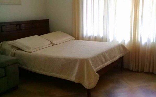A bed with a headboard, a bedside table, and a window with curtains. - Casa con Piscina Privada Anapoima (Anapoima)