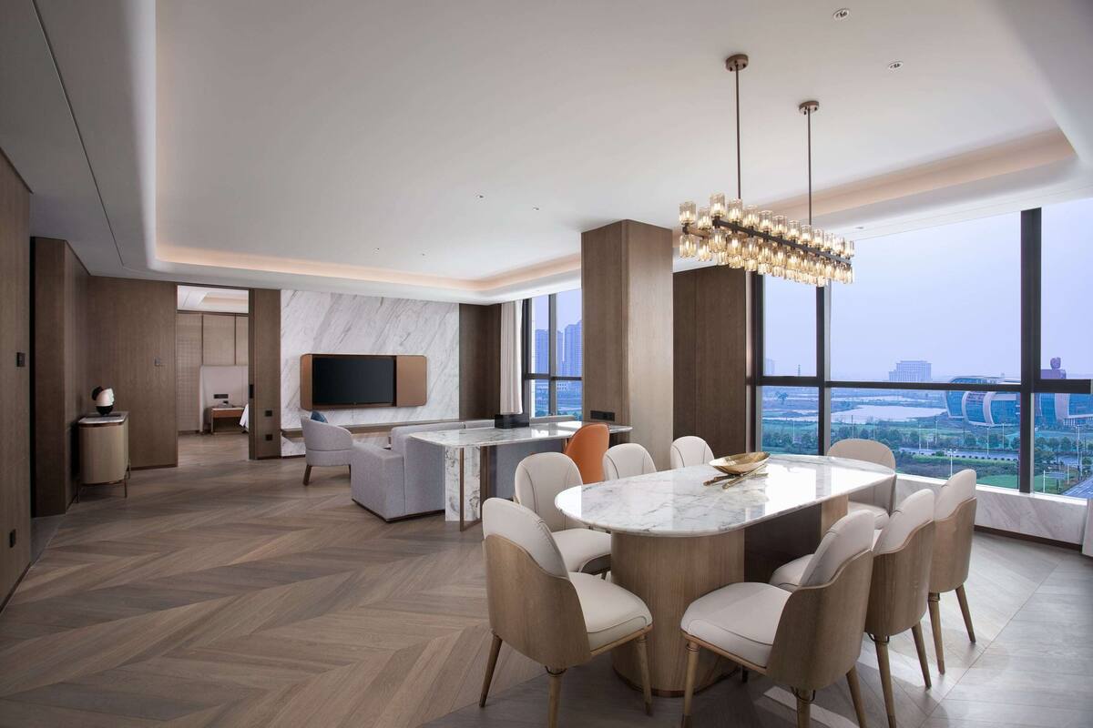 A modern living room with a large dining table, comfortable seating, a TV, and a city view.