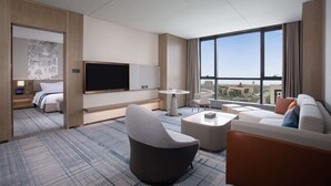 Una moderna camera d'albergo con una grande TV a schermo piatto, un divano confortevole, un'area pranzo e vista sulla città.