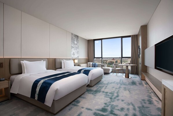 A hotel room with two beds, a desk, a chair, a TV, and a large window with a city view. - Wyndham Zhangshu (Yichun)
