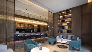 Una hall moderna con zone relax, un bar e un banco reception ben illuminato.