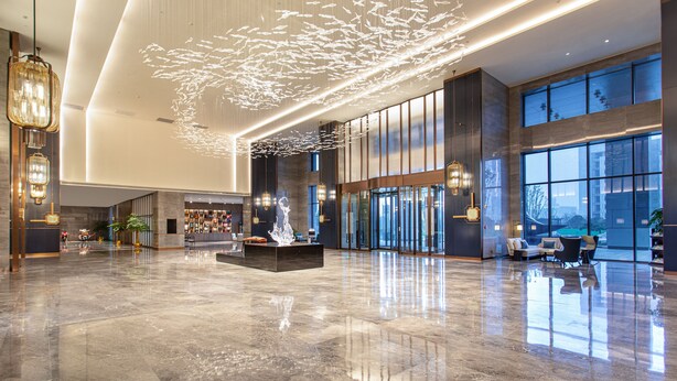 Un'ampia hall con pavimento riflettente, una fontana al centro e zone relax.