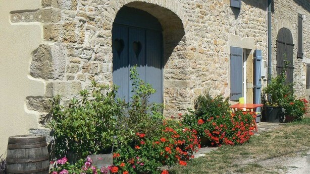 A stone building with arched doorways and a garden with red flowers.
