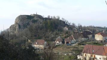 Un pueblo con casas en una ladera, una destacada formación rocosa y una estatua en la cima.