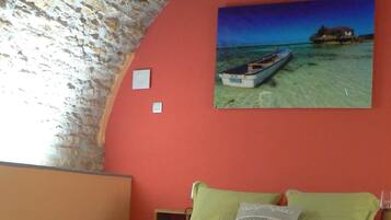 A bedroom with a red bedspread, a wooden headboard, a single bed, and a painting of a boat on a beach.