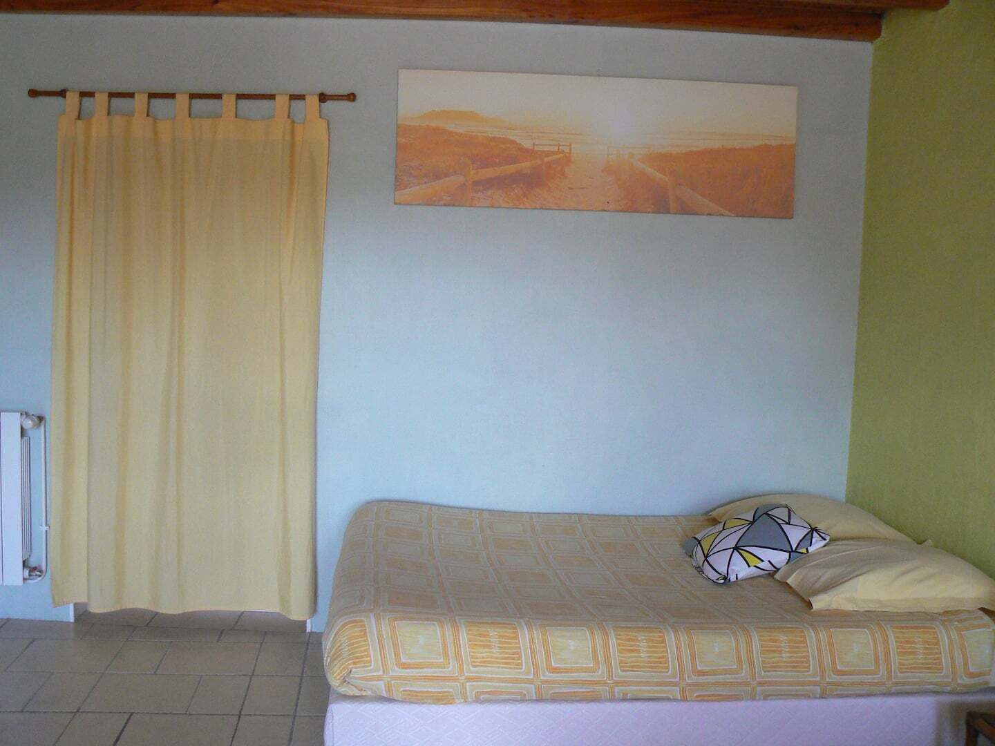 A bedroom with a bed, a curtain, a radiator, and a painting on the wall.