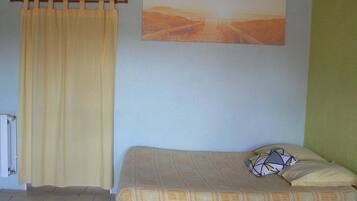A bedroom with a bed, a curtain, a radiator, and a painting on the wall.