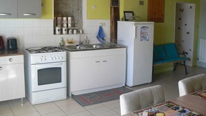 A compact kitchen with a gas stove, white cabinets, a refrigerator, and a dining area with a table and chairs.